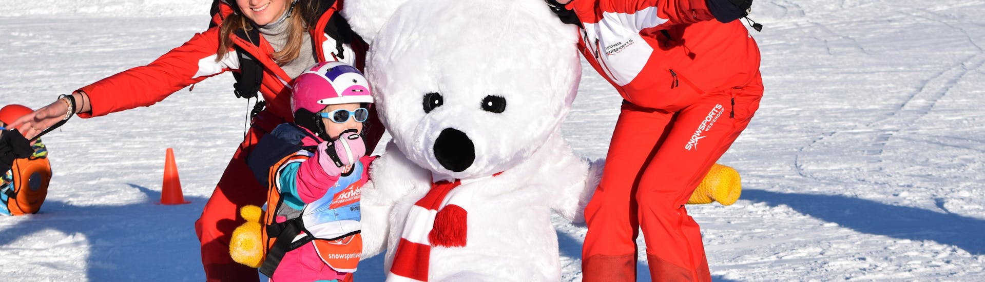 Two ski instructors, a child and Billy the polar bear during Kids Ski Lessons "Bambini" (3-4 y.) for All Levels with ski school Snowsports Westendorf.