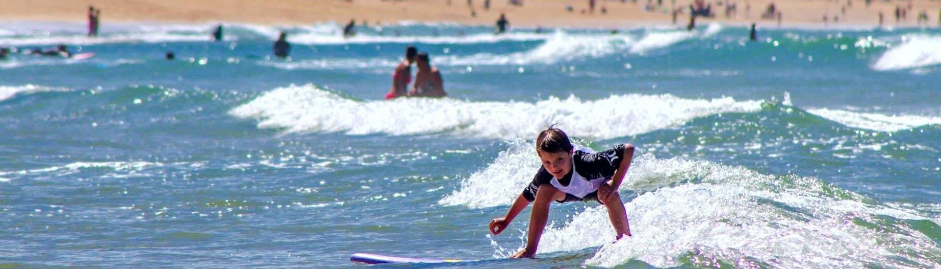 A young kid is surfing a wave thanks to his Surfing Lessons for Kids (6-11 years) - Culs Nus Beach with Hossegor Surf Center.