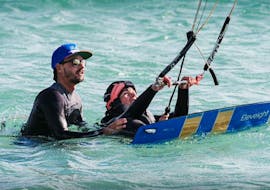 Un cliente de la escuela de kitesurf Addict está practicando lecciones semiprivadas de kitesurf para todos los niveles en el agua con su instructor en Tarifa.