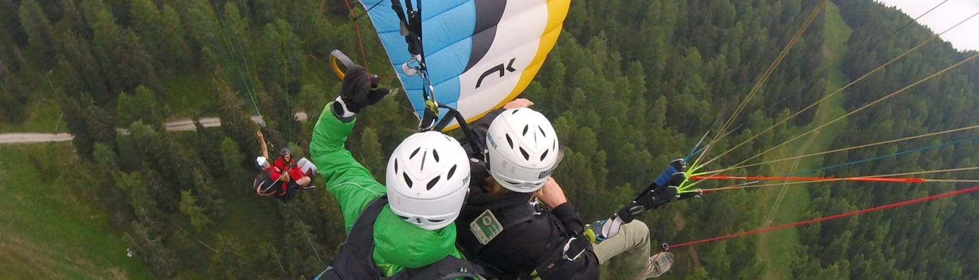 Während des Tandem Paragliding in Pfalzen bei Bruneck mit Tandemflights Kronplatz genießen eine junge Frau und ihr Tandempilot die spektakuläre Aussicht.