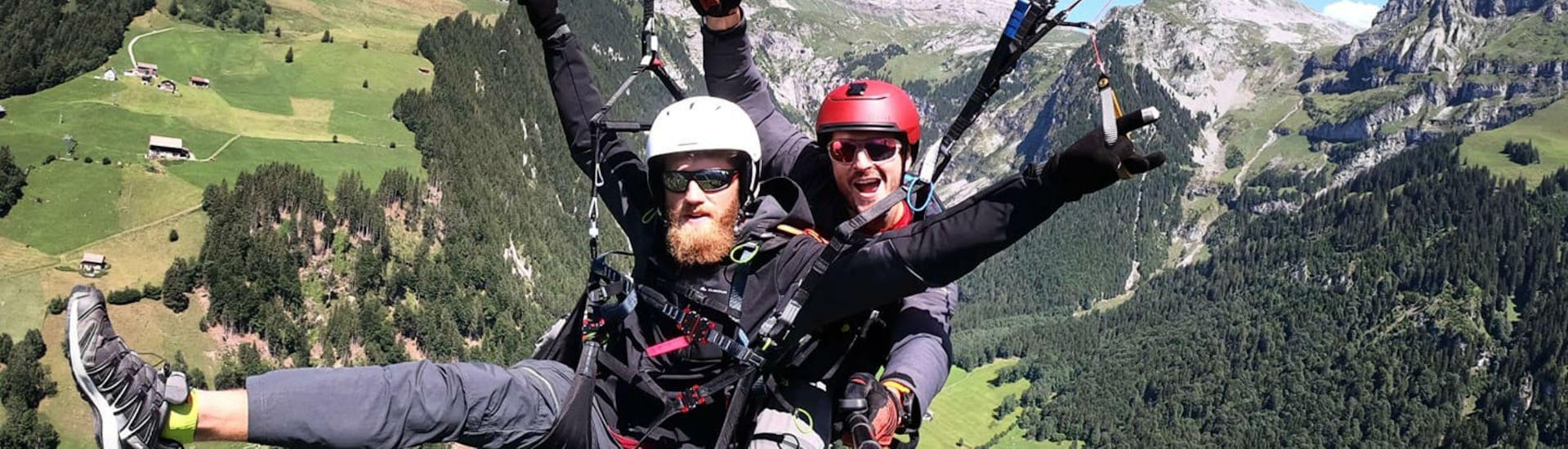 Ein Tandempilot von Mountain O'Clock und sein Passagier haben sichtlich Spaß während sie beim Paragliding am Vierwaldstättersee über die schweizer Berge fliegen.