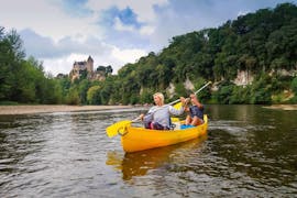 Ein Paar paddelt auf dem Dordogne vor einem Schloss während seiner 12 km langen Kanufahrt mit Canoës Loisirs Dordogne.
