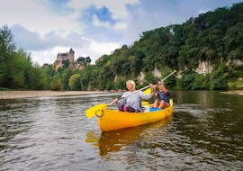 A couple are paddling on the Dordogne River in front of a castle during their 12 km canoe trip with Canoës Loisirs Dordogne.