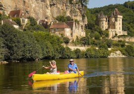 A couple is paddling on the Dordogne River in front of La Roque-Gageac during their 16 km canoe trip with Canoës Loisirs Dordogne.