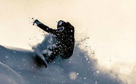 Een snowboarder rijdt een bocht en laat de sneeuw de lucht in spetteren tijdens de off-piste snowboardlessen - alle niveaus van de snowboardschool BOARD.AT.