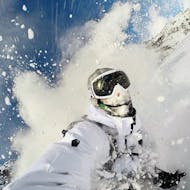 A snowboarder rides through a big cloud of snow and gives everything on the piste as part of the offer "Private off-piste Snowboard lessons - All Levels" of the snowboard school BOARD.AT.