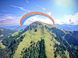 Ein Tandempilot von TirolAir und sein Passagier gleiten beim Paragliding von der Hohen Salve sanft über die Berggipfel der Kitzbüheler Alpen.