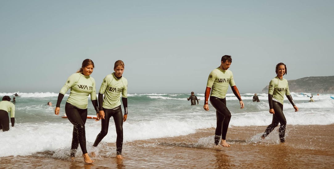 A group of people is walking along the beach during their Surfing Lessons near Lisbon with Wanted Surf School Carcavelos.