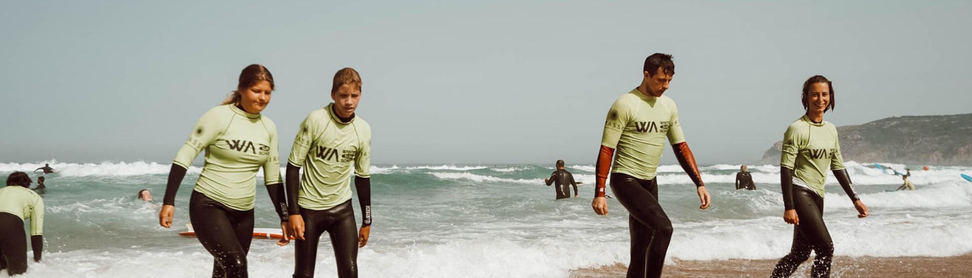 Eine Gruppe junger Leute geht beim Surfkurs nahe Lissabon mit Wanted Surf School Carcavelos den Strand entlang.
