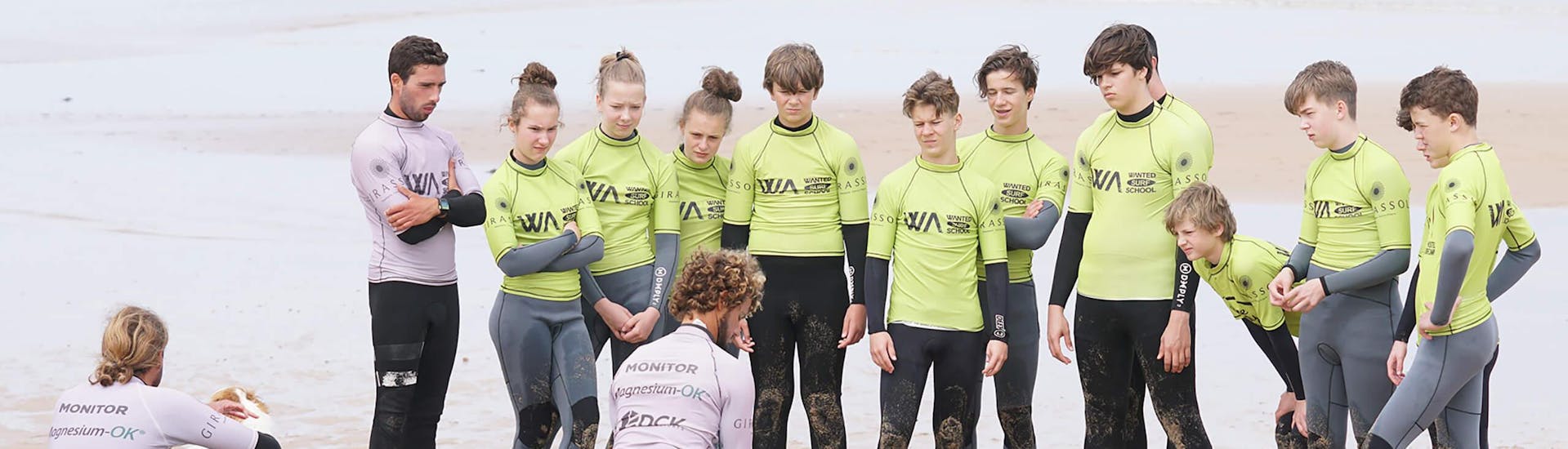 Un grupo de niños está viendo a su instructor de surf de Wanted Surf School Carcavelos demostrar cómo pararse en una tabla de surf durante sus clases de surf cerca de Lisboa.