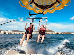 Two friends are sitting relaxed in the harness and are waiting to take off during the Parasailing in Cala Bona, offered by Sea Sports Mallorca.