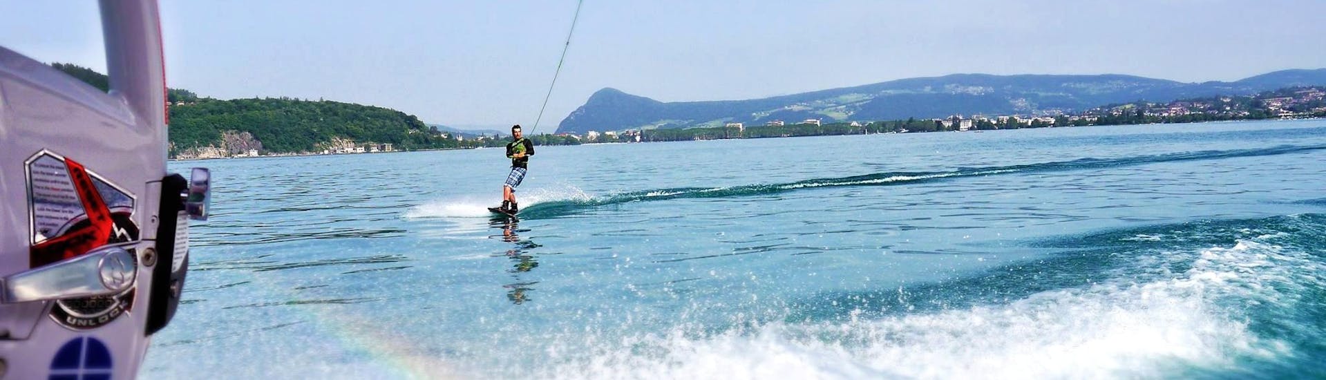 Un hombre aprovecha su alquiler de barco privado con Wakesurf & Wakeboard en el lago de Annecy para tomar una clase de wakeboard con Le Spot.