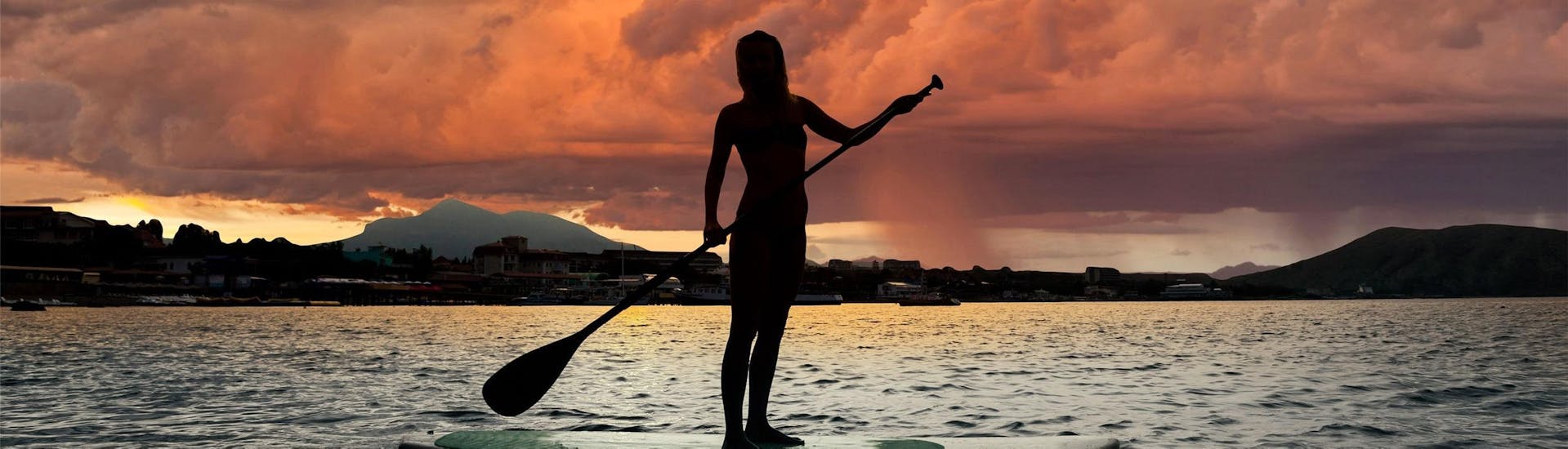 A woman is standing on a board at sunset and is enjoying her SUP Rental on Lake Annecy with Le Spot.