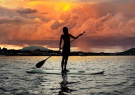 A woman is standing on a board at sunset and is enjoying her SUP Rental on Lake Annecy with Le Spot.