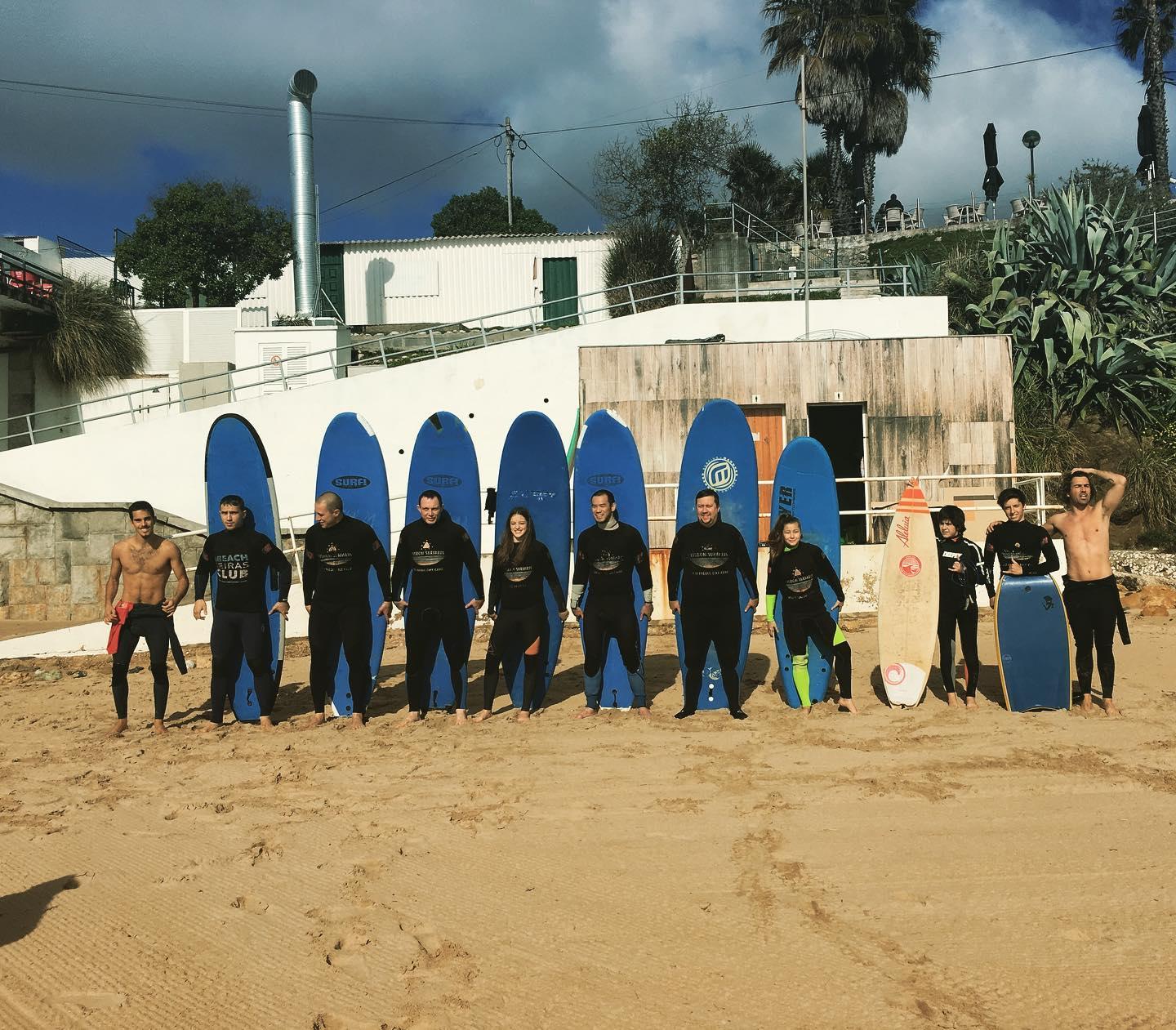 A group of aspiring surfers is posing for a photo alongside their surf instructors from Lisbon Surfaris before they get started with their private surfing lessons on Carcavelos Beach near Lisbon.