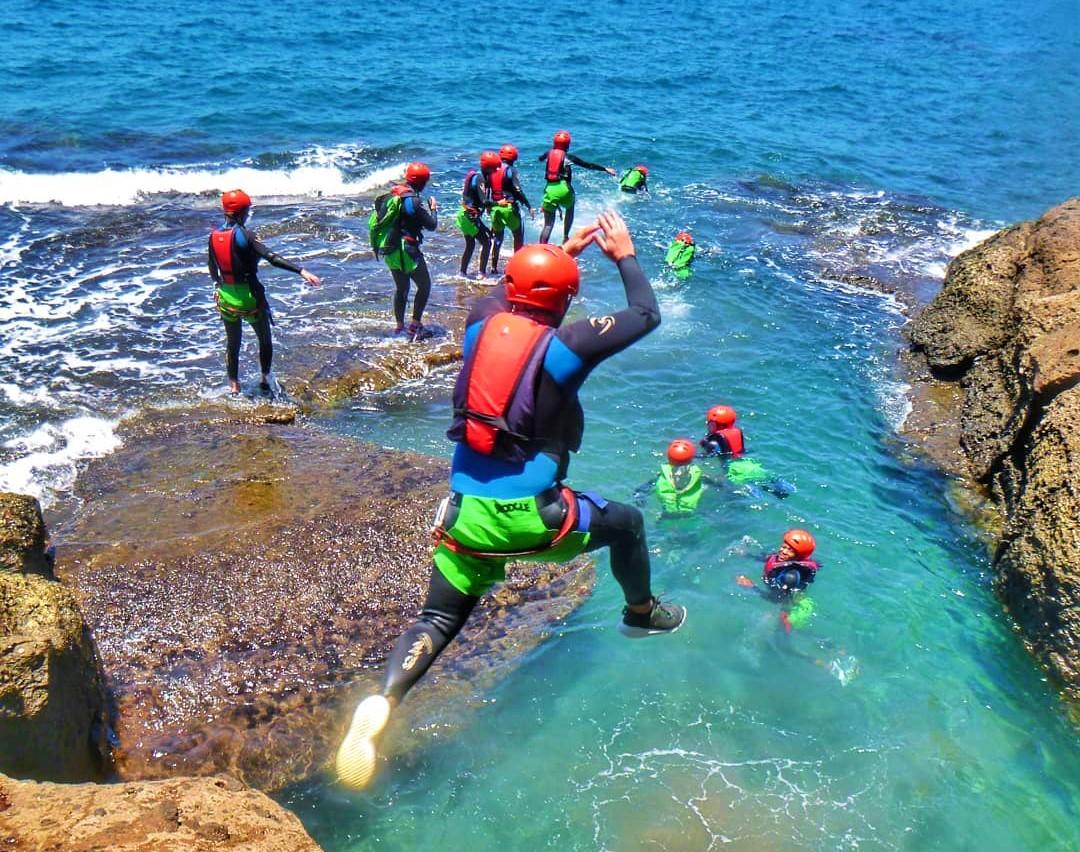 During the Coasteering at the South Coast of Gran Canaria, a man jumps from a rock into the crystal clear sea, under the supervision of a guide from Mojo Picón Aventura.