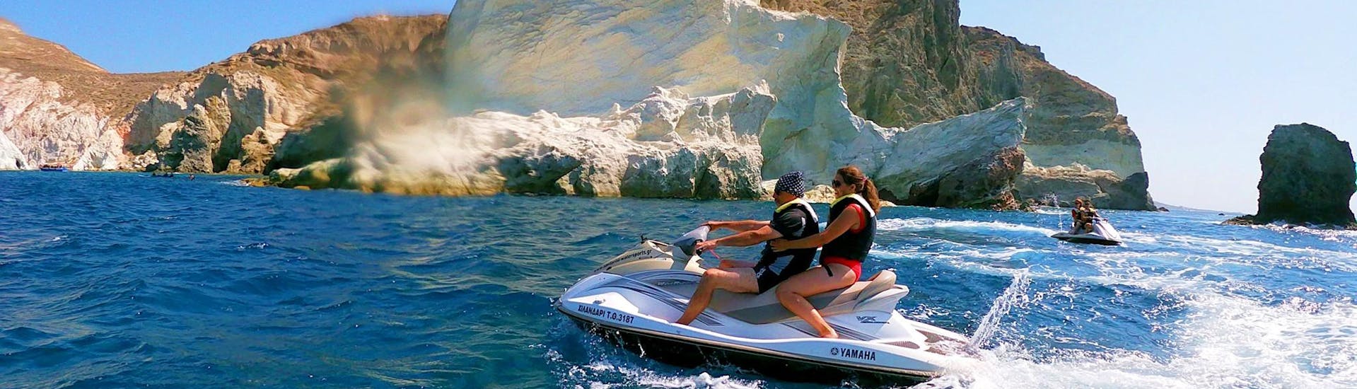 A couple is enjoying the ride across the waves during their Jet Ski Safari along the South Coast of Santorini with Kamari Beach Watersports Santorini.