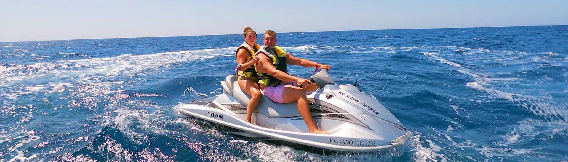 During the Jet Ski Safari to the Volcano & Hot Springs of Santorini with Kamari Beach Watersports Santorini, two participants are riding a Jet Ski across the blue water of the Aegean Sea.