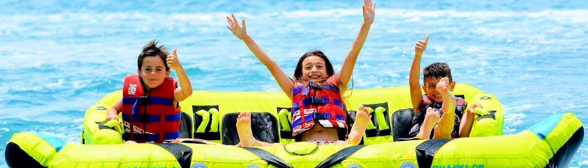 Drei Kinder haben viel Spaß bei ihrer Wasserschlauchbootfahrt am Kamari Beach in Santorini, die von Kamari Beach Watersports Santorini organisiert wird.