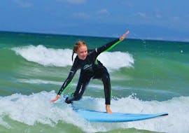 Ein junges Mädchen surft seine ersten Wellen während des Surfkurses an der Praia da Lagoa de Albufeira in Sesimbra mit Meira Pro Center Sesimbra.