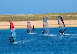 Four windsurfers are practicing their technique during the Windsurfing Lessons at Lagoa de Albufeira in Sesimbra under the guidance of an experienced intructor from Meira Pro Center.