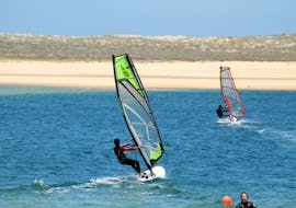 During the Private Windsurfing Lessons at Lagoa de Albufeira with Meira Pro Center Sesimbra, a windsurfer is riding over the water of the lagoon.