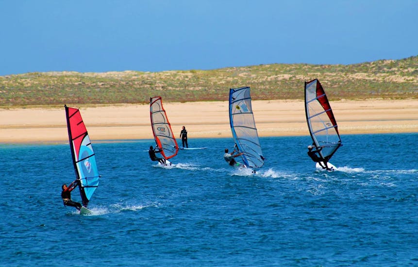 Four windsurfers are practicing their technique during the Private Windsurfing Lessons at Lagoa de Albufeira in Sesimbra under the guidance of an experienced intructor from Meira Pro Center.