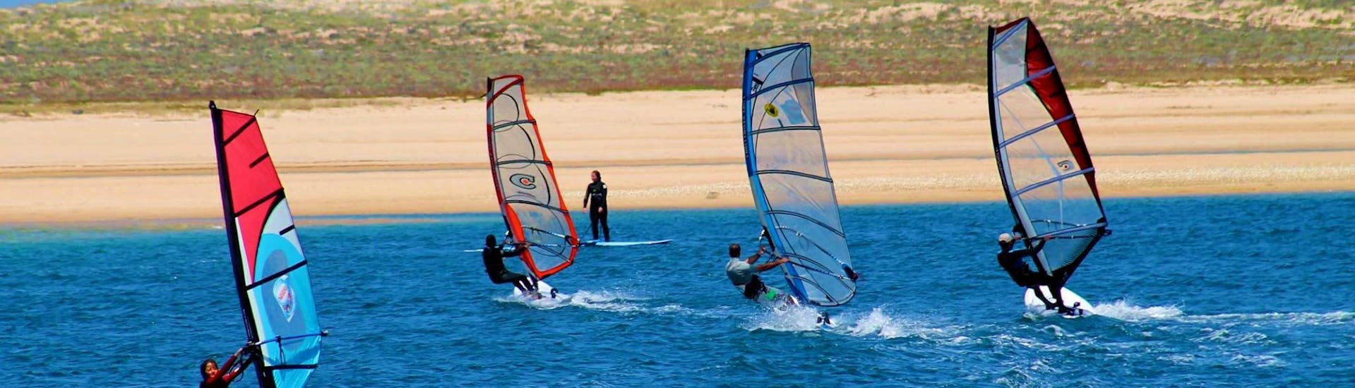 Vier Windsurfer üben während des privaten Windsurfkurses an der Lagoa de Albufeira in Sesimbra unter der Anleitung eines erfahrenen Intructors vom Meira Pro Center ihre Technik.