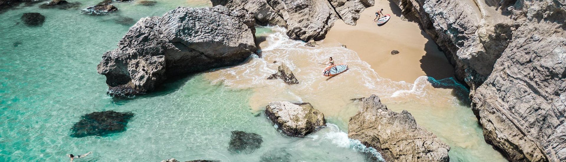 During their Private Boat Trip in Arrábida Natural Park from Sesimbra with Meira Pro Center Sesimbra, two friends are exploring a beach with the SUP boards available on board.