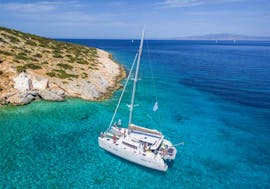 The catamaran Apollon from Naxos Catamaran is sailing along the rocky coast of the Cyclades during the Private Sailing Cruise on a Luxury Catamaran from Naxos.