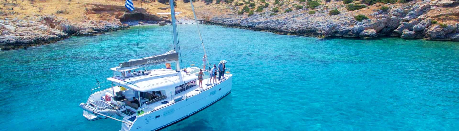 The catamaran Apollon from Naxos Catamaran is sailing along the rocky coast of the Cyclades during the Private Sailing Cruise on a Luxury Catamaran from Naxos.