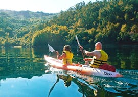 A couple is paddling across the waters of the Caniçada reservoir while kayaking in the Peneda-Gerês National Park with Oporto Adventure Tours.