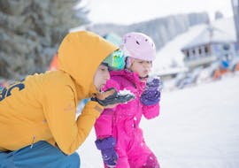 Een meisje vermaakt zich in de sneeuw met een instructeur van NTC Sport Skischule Oberstdorf tijdens privé skilessen voor kinderen voor beginners.