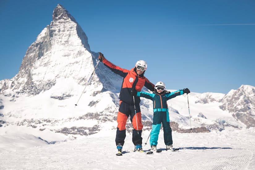 Een skileraar en een kind juichen tijdens de Kids Skilessen (6-11 j.) voor alle niveaus.