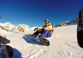 Ein Snowboarder sitzt entspannt im Schnee und genießt die schöne Aussicht während dem Snowboardkurs für Kinder & Erwachsene aller Levels von Life Ski Escuela de Esquí Baqueira.