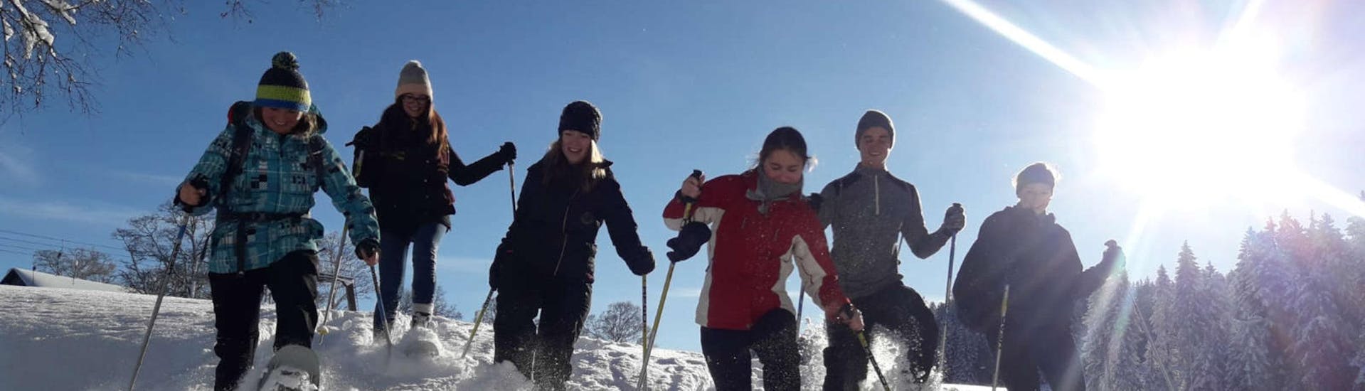 Eine Gruppe junger Menschen hat sichtlich Spaß während sie bei ihrer privaten Schneeschuhwanderung mit der Skischule Schwarzenberg am Bödele durch den Tiefschnee stapft.