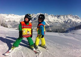 Zwei Kinder stehen glücklich auf der Piste und freuen sich im Rahmen des Privater Kinder-Skikurs (ab 3 J.) für alle Levels von Skischule Ingrid Salvenmoser über ihren Lernfortschritt.