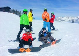 Een groep snowboarders zit ontspannen in de sneeuw en neemt een pauze tijdens de privé snowboardlessen voor kinderen en volwassenen van alle niveaus van de Skischool Ingrid Salvenmoser.