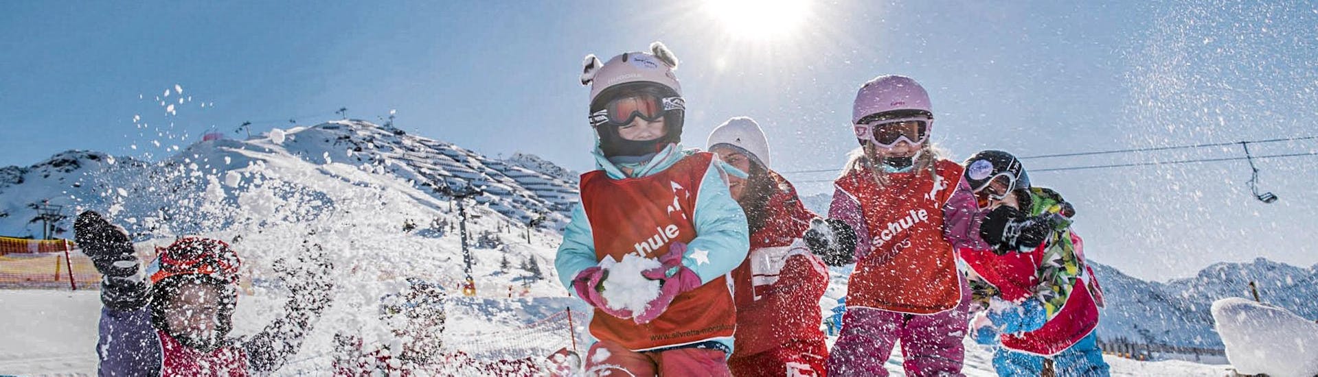 Un groupe de jeunes enfants s'amuse lors d'une bataille de boules de neige pendant leur cours de ski pour enfants Bambini (3-5 ans) pour débutants avec la Skischule Schruns.