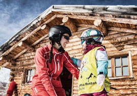 Eine Skilehrerin unterstützt im privaten Kinder-Skikurs für alle Altersgruppen ein junges Kind bei seinen ersten Erfahrungen auf Skiern.