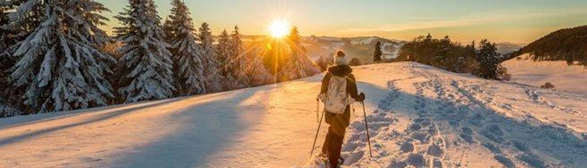 A lone hiker is watching the sunset while on their private snowshoeing tour with ACT-Sports Skischule in Arosa.