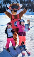 Two young girls receive their medal and certificate from mascot Foxy after they completed their Kids Ski Lessons (from 4 y.) for All Levels with Skischule Tannberg Lech.