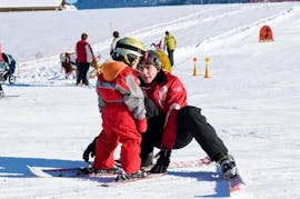 Een jong kind zet zijn eerste stappen in de sneeuw dankzij de hulp van een skileraar van de skischool ESS Château d'Oex tijdens hun privéskilessen voor kinderen voor beginners.