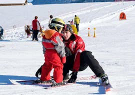 Een jong kind zet zijn eerste stappen in de sneeuw dankzij de hulp van een skileraar van de skischool ESS Château d'Oex tijdens hun privéskilessen voor kinderen voor beginners.