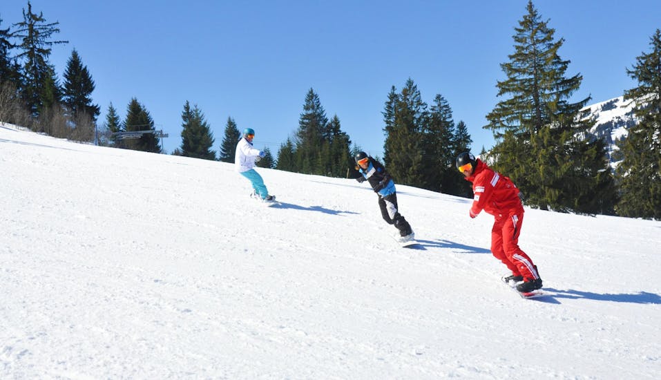 Snowboarders volgen hun snowboardleraar op de piste tijdens hun privé-snowboardlessen voor alle niveaus bij de skischool ESS Château d'Oex.