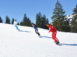Los snowboarders siguen a su instructor de snowboard en la pista durante sus clases particulares de snowboard para todos los niveles, con la escuela de esquí ESS Château d'Oex.