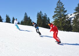 Snowboarder folgen während ihres Snowboardkurse für alle Levels mit der Schweizer Skischule Château d'Oex ihrem Snowboardlehrer auf der Piste.