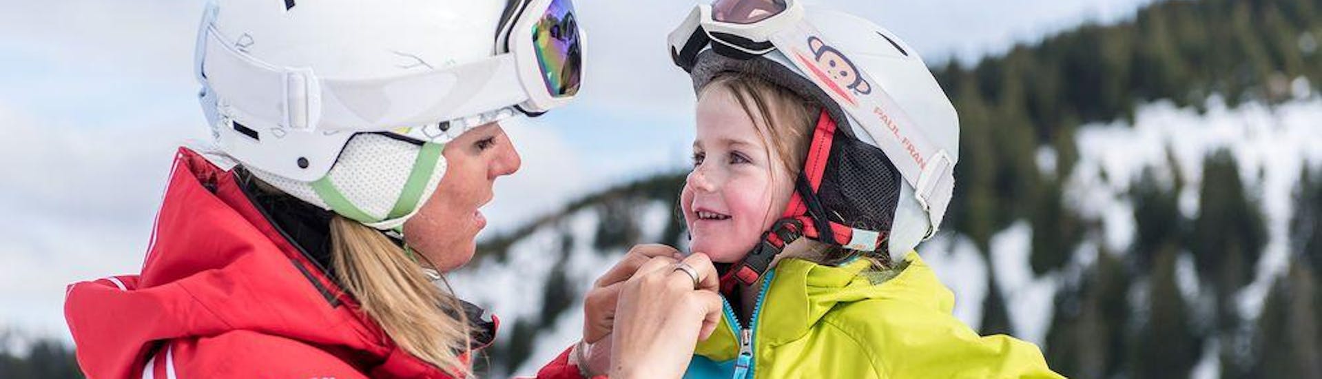 Un moniteur de ski aide son jeune élève à mettre son casque pendant son Cours particulier de ski Enfants pour Tous âges avec l'école suisse de ski Wildhaus.