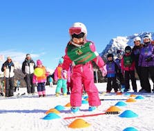 Una bimba si diverte di fronte alla scuola Maestri di Sci Moena dopo le Lezioni di sci per bambini (4-14 anni) per tutti i livelli.
