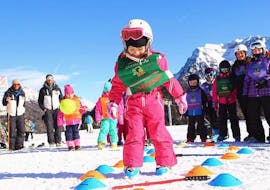 Una bimba si diverte di fronte alla scuola Maestri di Sci Moena dopo le Lezioni di sci per bambini (4-14 anni) per tutti i livelli. 